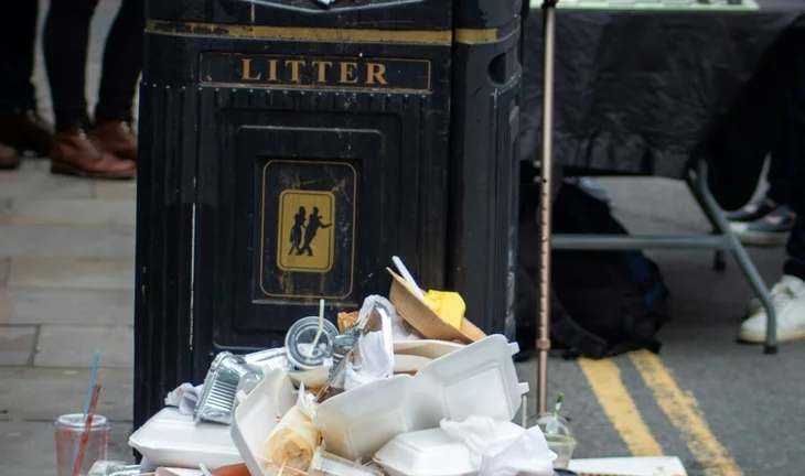 A black litter bin with litter piled up 